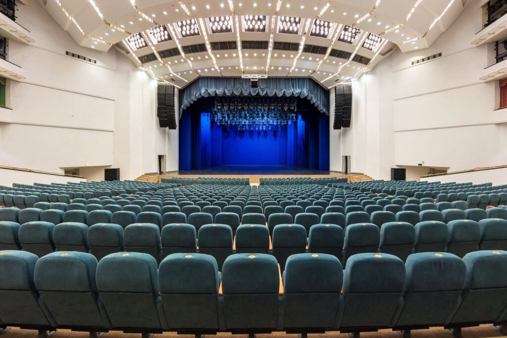 Interior of a white conference concert hall or theatre with blue scene and green seats